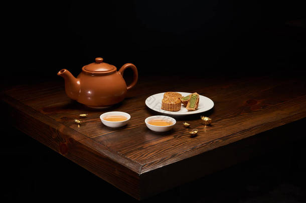 茶壶, 月饼和杯在木桌上隔离在黑色