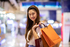 美丽迷人迷人快乐的亚洲女人笑着在商场里提购物袋，享受购物的乐趣