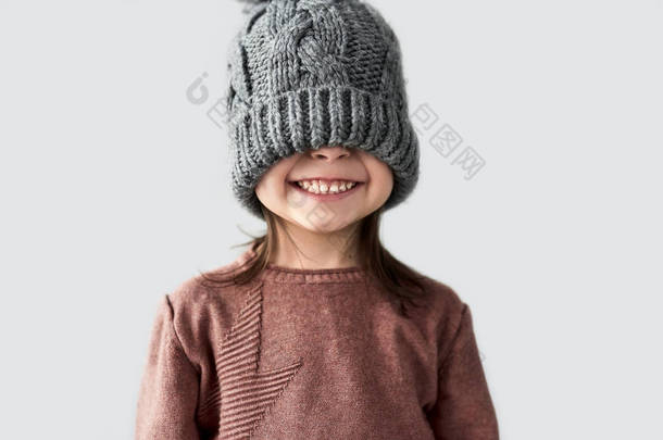 有趣的女孩隐藏的眼睛在<strong>冬天</strong>温暖的灰色帽子, 微笑着, 穿着毛衣 
