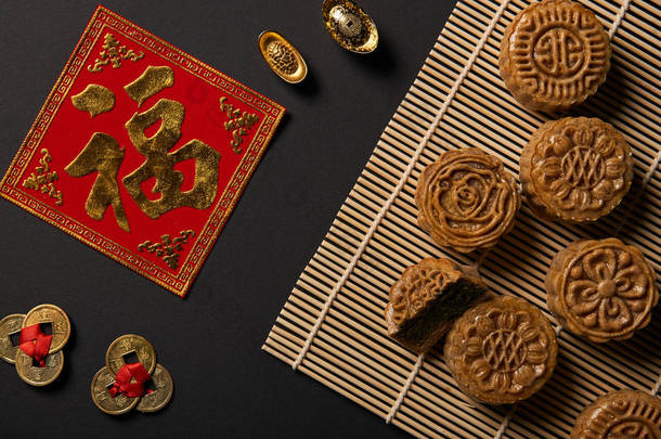 在黑色上查出的传统月饼和中国护身符和竹桌垫的顶视图