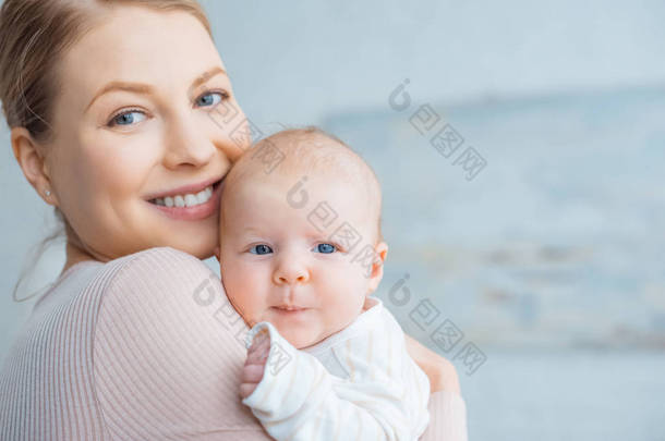 快乐的年轻母亲抱着可爱的婴儿, 对着镜头微笑