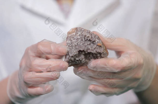 明亮的灰色红宝石水晶矿石在手与手套。结晶是实验室中固体形成的自然或人工过程.
