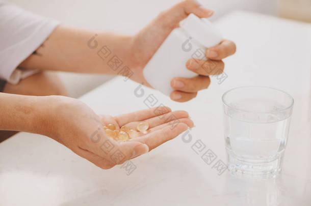 手与黄色胶囊欧米茄 3, 白色药丸的氨基葡萄糖和钙在塑料盒, <strong>玻璃</strong>与<strong>水</strong>在木桌上, 顶部视图.