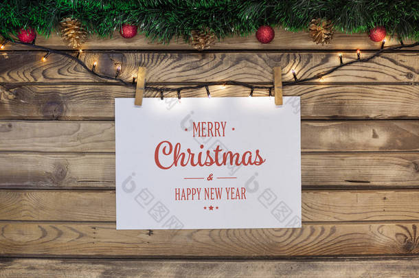 圣诞问候在一个白色的床单上挂着一个花环与 clothespins 在一个木质的背景上装饰绿色的金属丝和红色的玩具