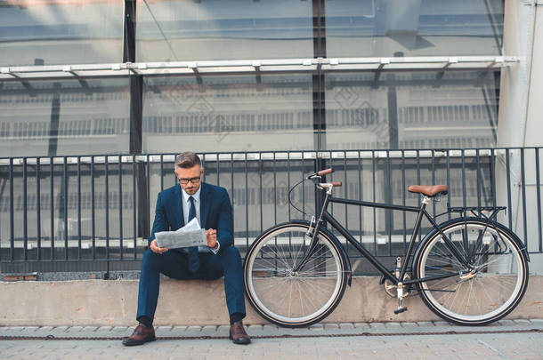 <strong>中年</strong>商人看报纸, 而坐在自行车附近的街道上 