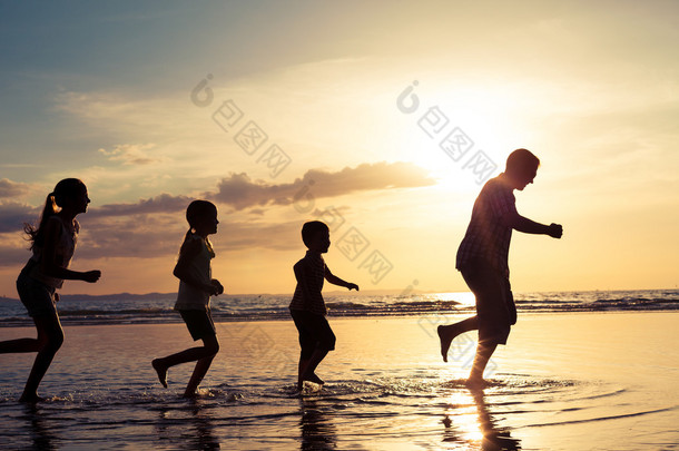 父亲和孩子们在日落的时候在海滩上玩.