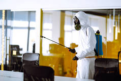办公室消毒以防止COVID-19，穿着防护服的男子用喷雾剂化学品，以防止大肠病毒在检疫城市的蔓延。清洗概念.