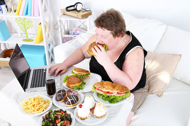 胖男人有一顿大餐和家居室内背景上的笔记本电脑上玩游戏  