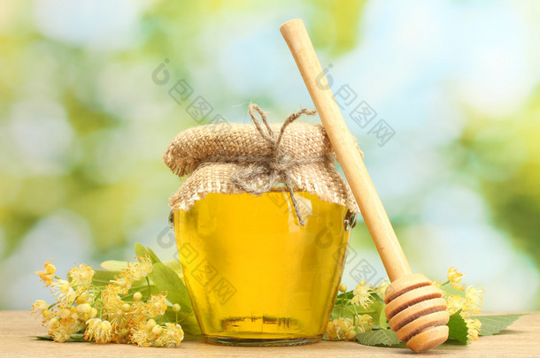 jar 椴树蜜和绿色背景上的木桌上的花