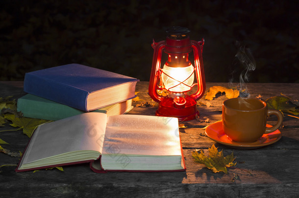 书的翻开，灯和一杯热咖啡放在黑暗的森林的旧木桌上。落黄枫叶。复古和古老的概念。秋天的心情.