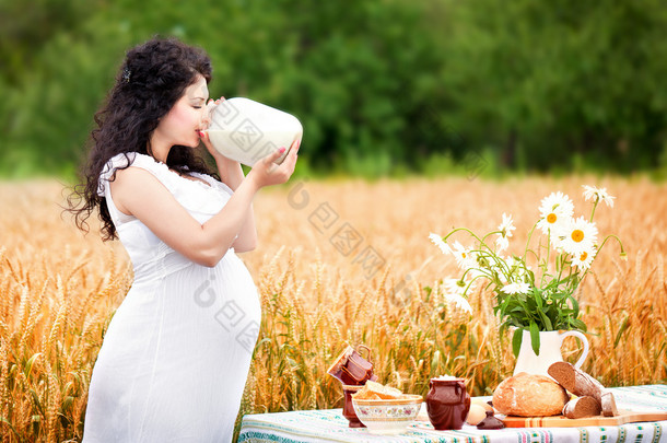 可爱的怀孕女孩喝牛奶在一个字段中