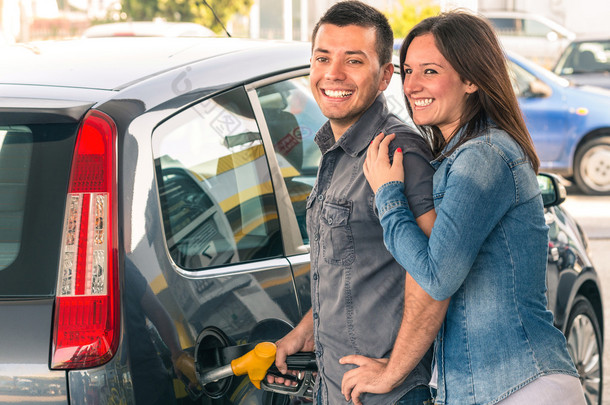 幸福的情侣在加油站的加油泵抽汽油。年轻的男人和男人的女人肖像在油箱加注现代汽车