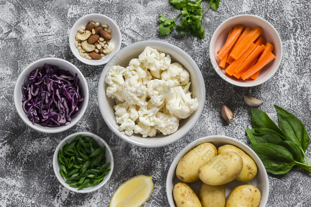 各种新鲜蔬菜在碗-土豆、 红和花椰菜、 菠菜、 大葱、 胡萝卜、 坚果、 橄榄油、 香菜。原料。素食主义者表。顶视图