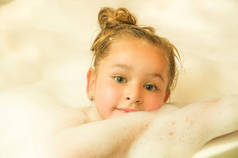 在浴缸中与水和泡沫浴中的构成的美丽小姑娘