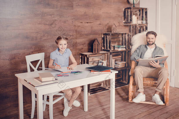 做家庭作业和坐在桌旁，父亲拿着本书坐在身后的小女孩