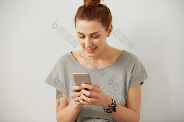 一个微笑的年轻女子使用手机的肖像。美丽的快乐女孩聊天和<strong>短信</strong>在灰色背景的手机。年轻女子在智能手机上阅读<strong>短信</strong>