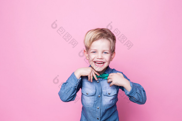 年轻英俊的小伙子笑着，穿着蓝色的衬衫，打着蝴蝶领带。粉红<strong>背景</strong>的工作室肖像