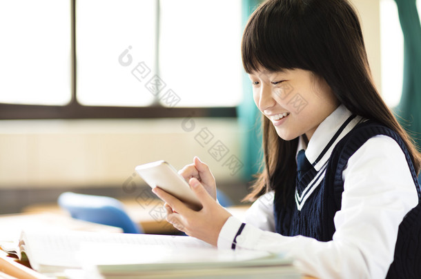 智能手机在教室里的女孩快乐的学生