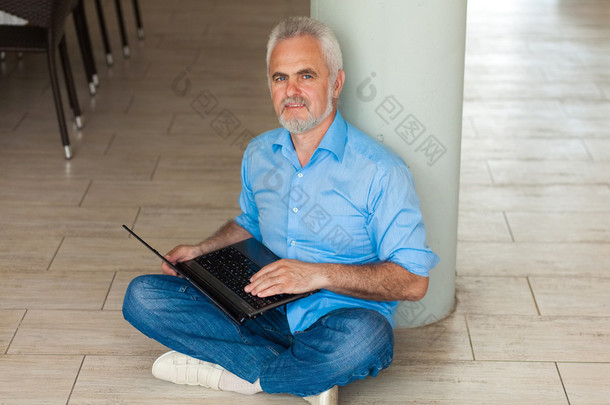 老人用笔记本电脑坐在地板上