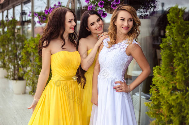 美丽的<strong>新娘</strong>和黄色相似的连衣裙上一个夏天在一起的两个伴娘露台海上餐厅