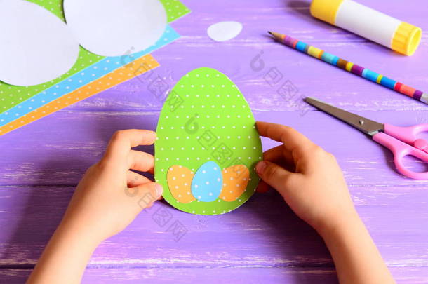 小孩子手里拿着复活节纸卡.孩子们制作了有创意的彩蛋形复活节贺卡.在木制桌子上进行艺术活动的材料.幼稚园或家中手工造纸工艺概念