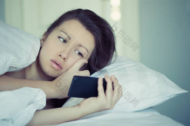 一个漂亮的女孩躺在床上，不能入睡并读取在智能手机上的新闻。失眠。心理学。恐惧症