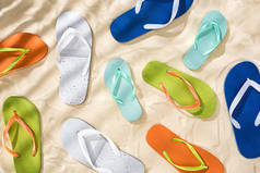 散落的白色、绿松石色、绿色和蓝色拖鞋的顶视图，带阴影的沙上