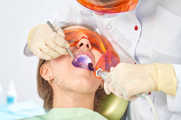 Girl child at the doctor. Dentist places a filling on a tooth with dental polymerization lamp in ora