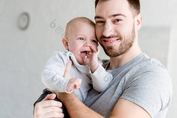 年轻的微笑的父亲抱着小男孩在家里  
