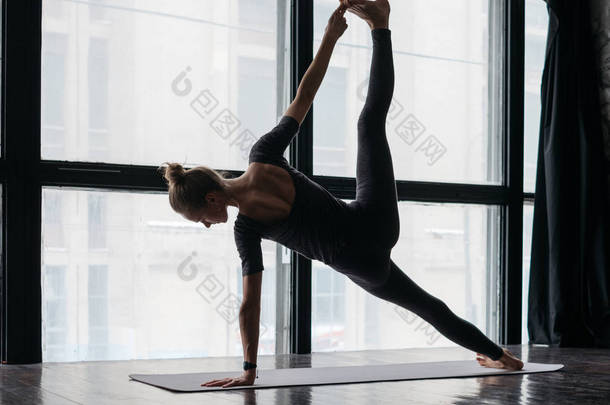 年轻灵活的<strong>运动</strong>妇女在木地板上的窗户附近练习瑜伽