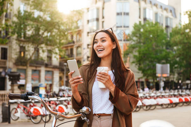 女孩的形象户外自行车在街上看着一边聊天的手机喝咖啡.