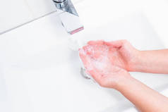 用人的肥皂和水洗手以防止考拉韦病毒，卫生以防止考拉韦病毒的传播。女人用肥皂在水龙头下洗手。手部卫生概念细节.