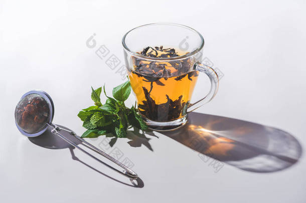 杯红茶, 薄荷和茶叶过滤器在白色桌面上 