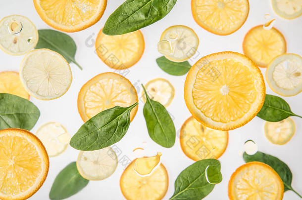 新鲜的橘子和柠檬片与绿色菠菜叶在灰色的背景