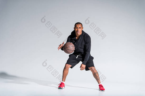 运动的非洲裔美国人男子打篮球球和看在灰色相机