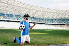 职业足球运动员，头戴假发，身穿蓝白相间的球衣，膝盖着地，在体育场的足球场上摆出肯定的手势