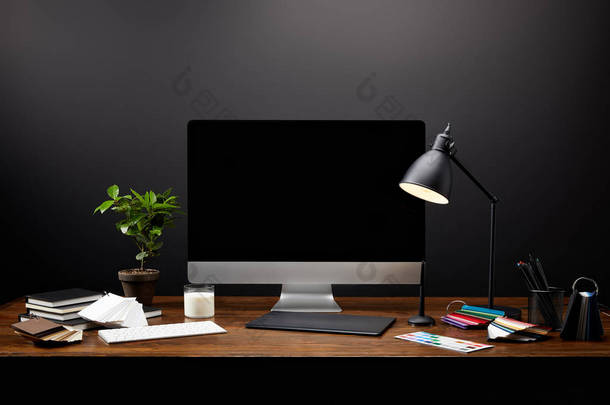 在木制桌面上用图形片、空白电脑屏幕、笔记本和托盘关闭图形设计师工作场所的视图