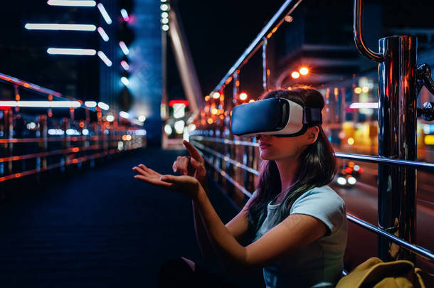 虚拟现实中的年轻女子耳机坐在街上与夜间城市背景