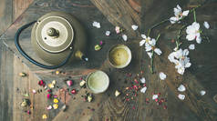 传统的亚洲茶道安排。铁茶壶, 杯子, 干玫瑰花蕾和盛开的杏仁树花在木桌背景上