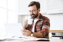年轻留着胡子的男人戴着眼镜边喝茶边在家里做笔记的画像