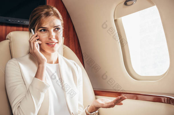 穿着西服的漂亮女商人在私人飞机上用智能手机交谈 