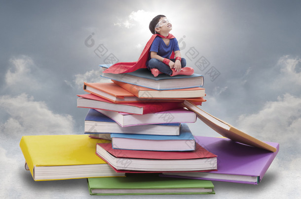 超级英雄男孩坐在书堆上