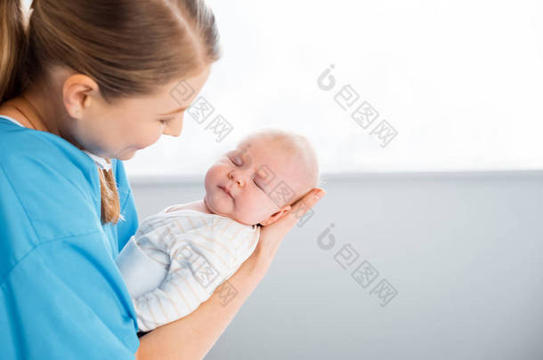 幸福的<strong>年轻</strong>母亲在病房里抱着<strong>可爱</strong>的熟睡婴儿的侧视图