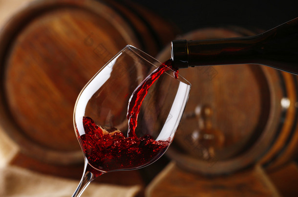从瓶的红酒注入玻璃与葡萄酒木桶上背景