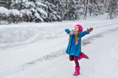 小女孩穿着一件蓝上衣和粉红色的帽子和靴子，到了冬季的森林里，伸出两臂运行