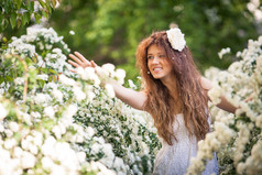 美丽的小姐带迷人的微笑，在春天满白色花朵的花园