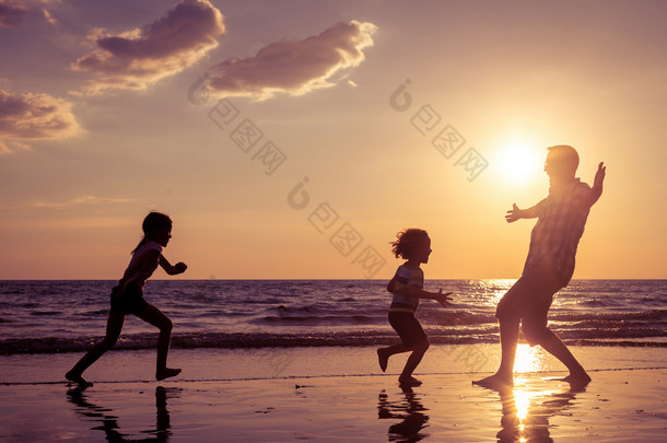 父亲和<strong>孩子</strong>们在日落的时候在海滩上玩.