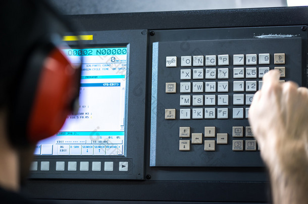 Cnc 操作员、 机械技师在金属加工铣削中心与键盘戴降噪耳机插入数据的工具车间工人
