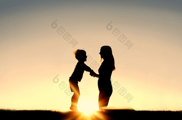 母亲和年幼的孩子，手牵着手在日落时的<strong>剪影</strong>