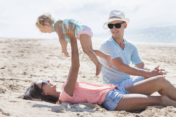 年轻的父母在海滩上玩他们的小女儿